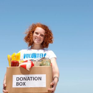 Volunteer holding a donation box, smiling outside.